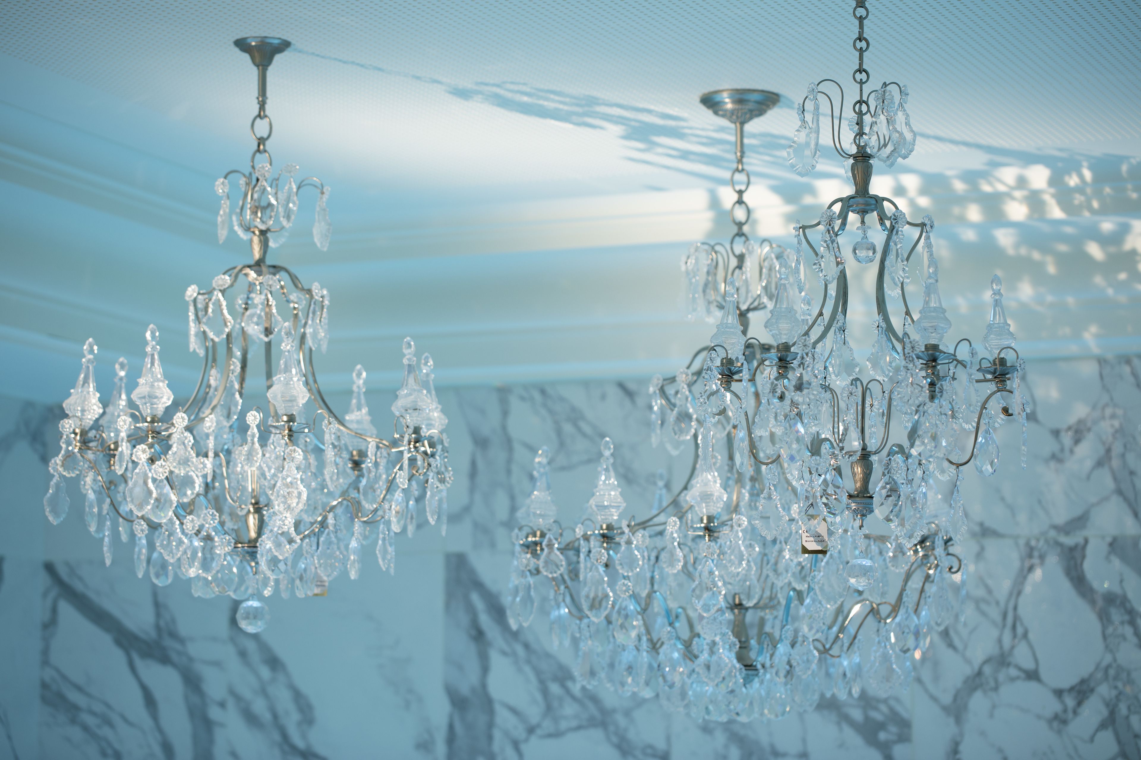 Two crystal chandeliers hanging from the ceiling in a room with a marble wall.