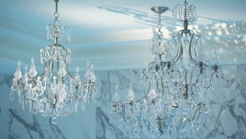 Two crystal chandeliers hanging from the ceiling in a room with a marble wall.