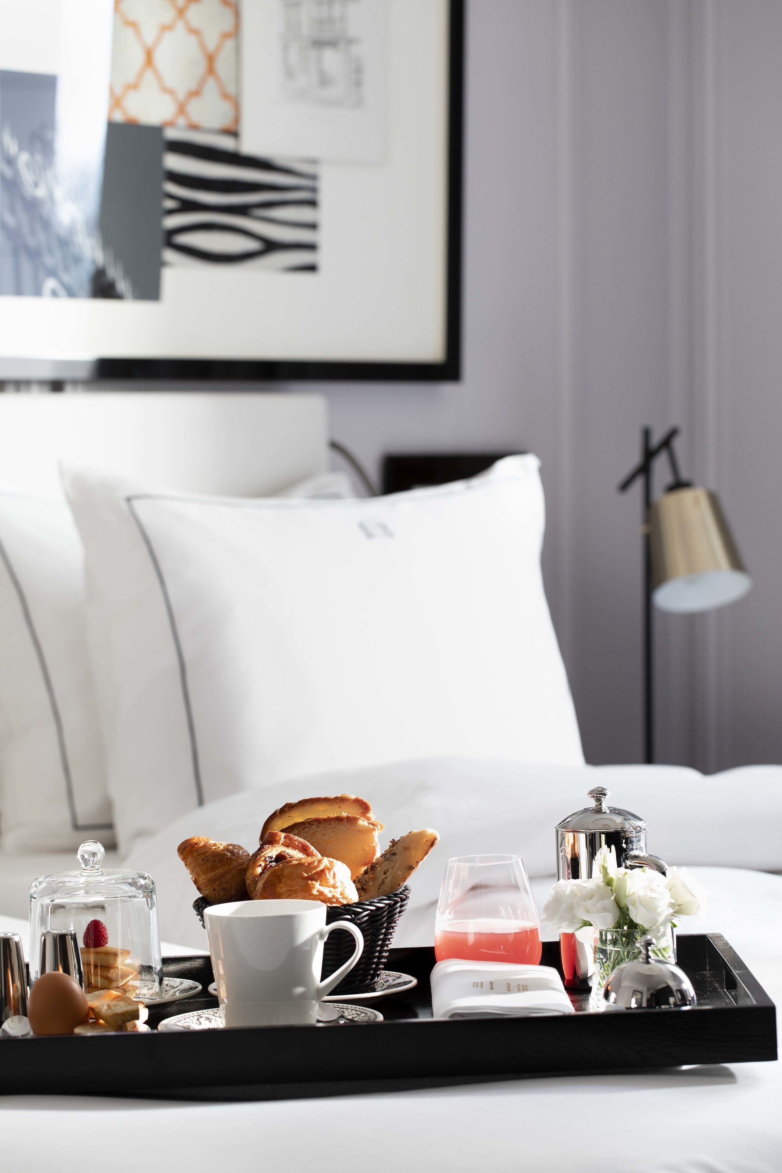Una bandeja de desayuno ordenada sobre la cama, con pastelería, una taza y un vaso de bebida rosada.