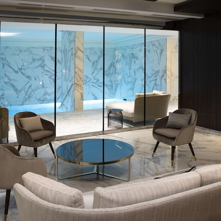 A modern lounge area with a glass coffee table, comfortable seating, and a view of the sea through large glass windows.