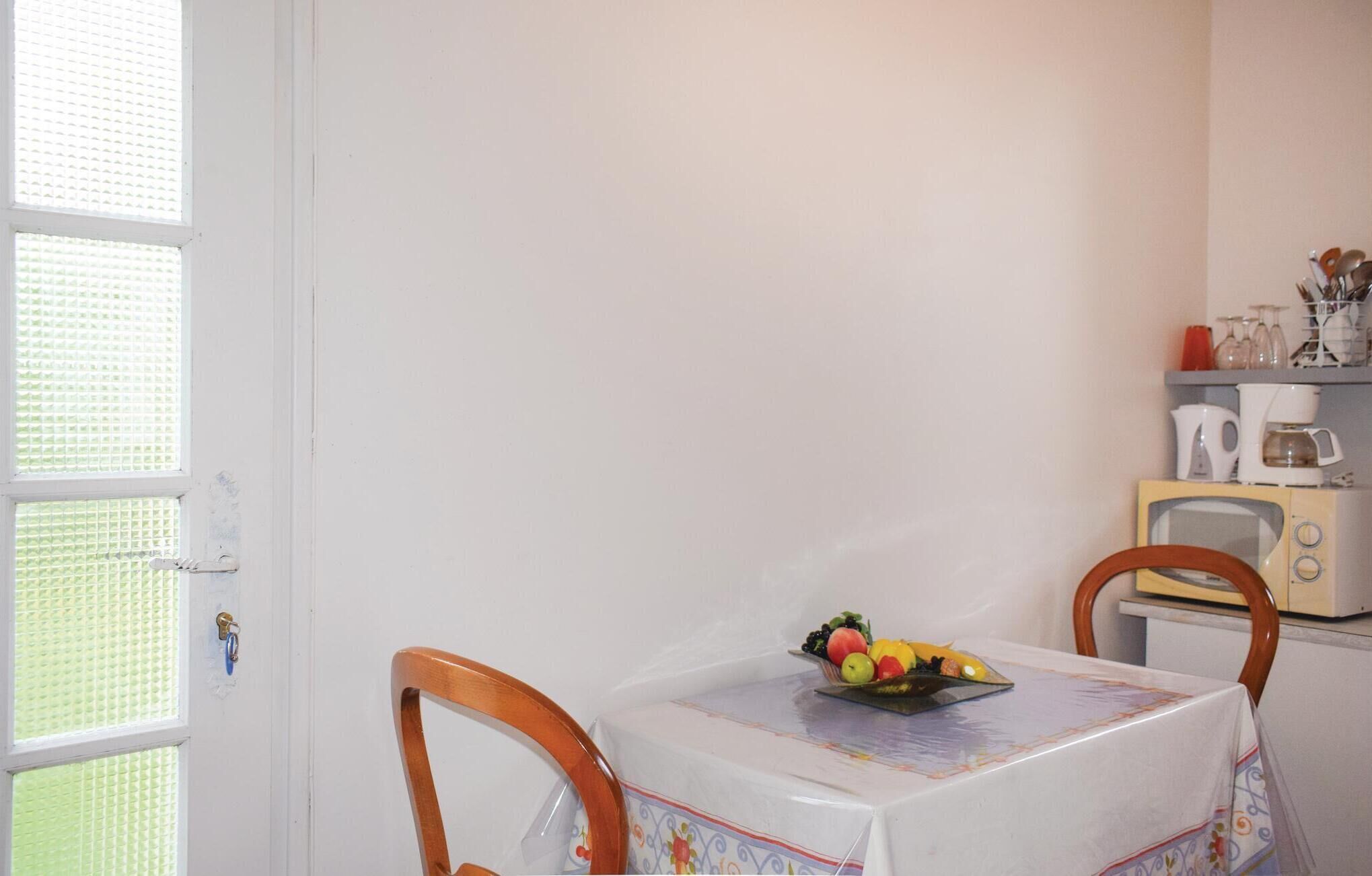 A small kitchen with a table set for two, a fruit bowl on the table, and a vintage toaster oven on the counter.