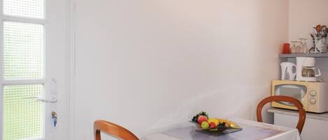 A small kitchen with a table set for two, a fruit bowl on the table, and a vintage toaster oven on the counter.