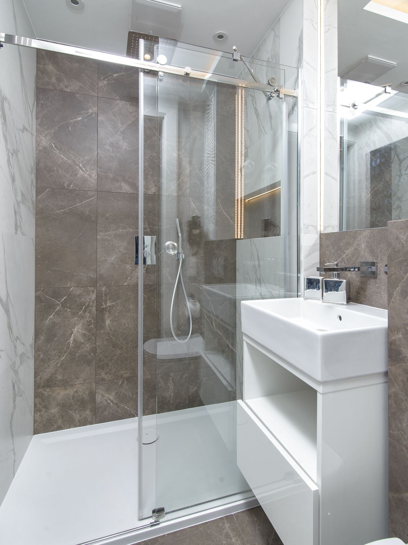 A modern bathroom with a glass-enclosed shower, marble walls, and a white vanity.