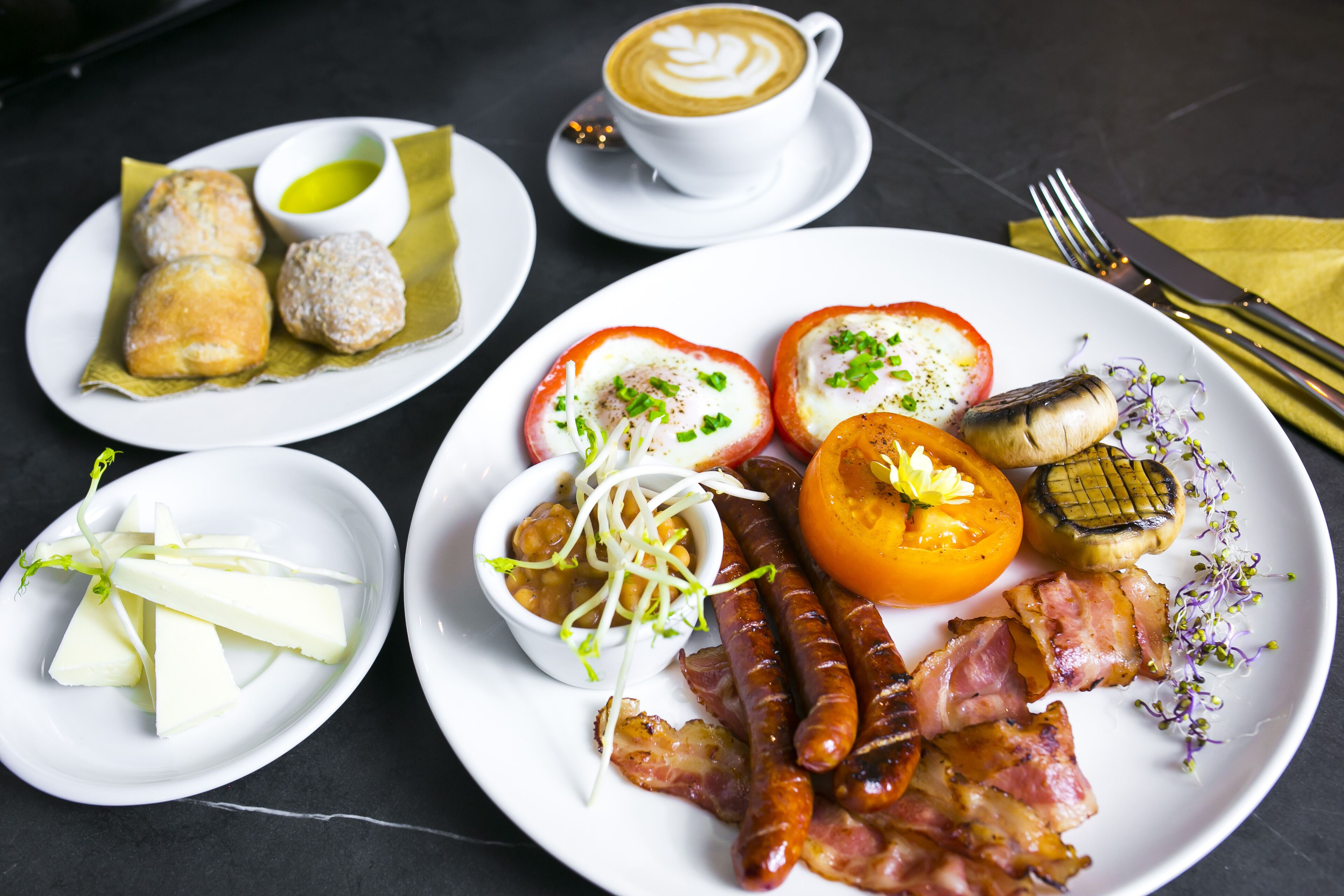 Un plato de desayuno con salchichas, tocino, tomates y una taza de café.