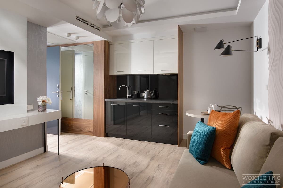 Eine moderne Küche mit dunklen Schränken, ein Essbereich mit rundem Tisch und ein Wohnzimmer mit einer Couch und Kissen.