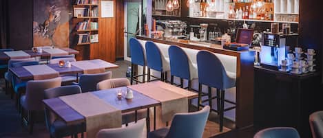 Un restaurante con varias mesas y sillas, una zona de bar con una máquina de café y una estantería con libros.