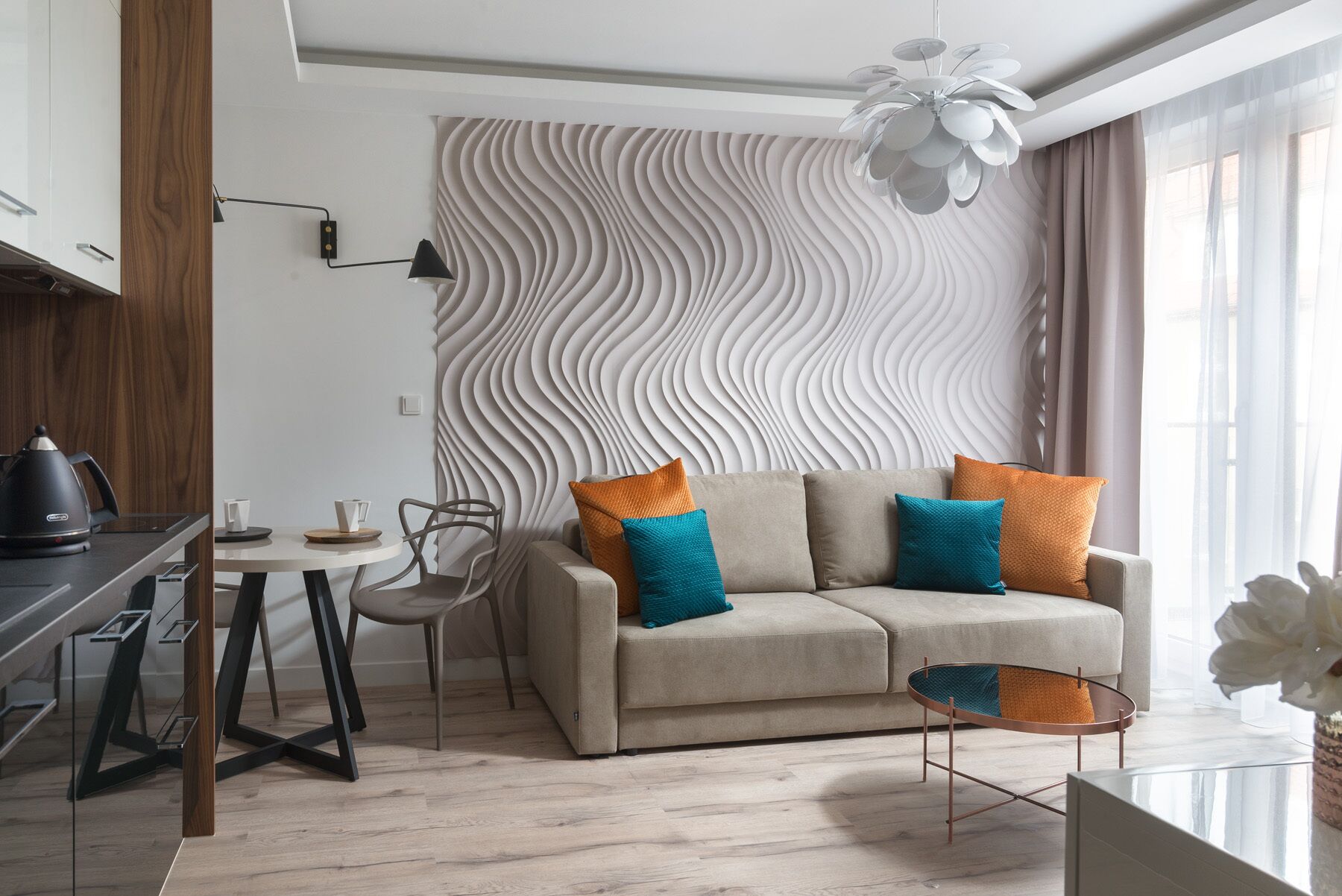 A modern living room with a sofa, a coffee table, and a dining area with a kettle and cups.