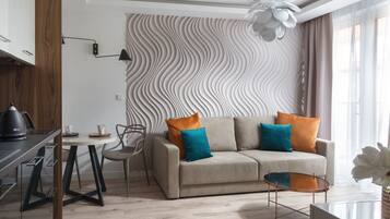 A modern living room with a sofa, a coffee table, and a dining area with a kettle and cups.