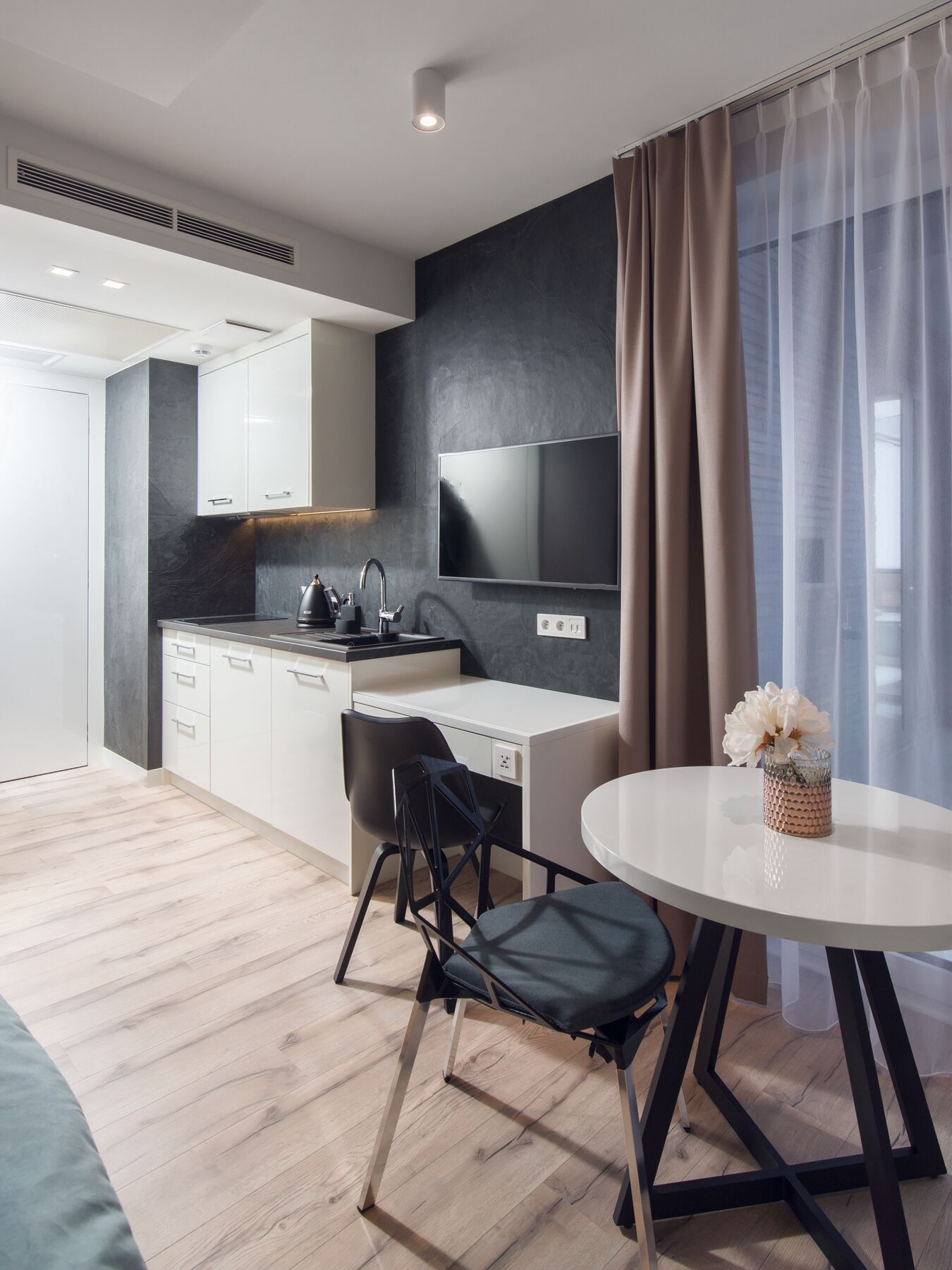 A modern kitchen with white cabinets, a black countertop, and a built-in stove. There is a dining area with a round table and two chairs.