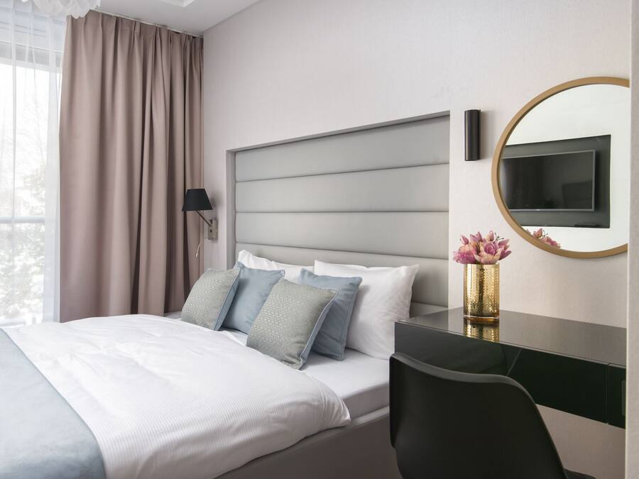 A modern hotel room with a large bed, a desk, a chair, a TV, and a mirror.