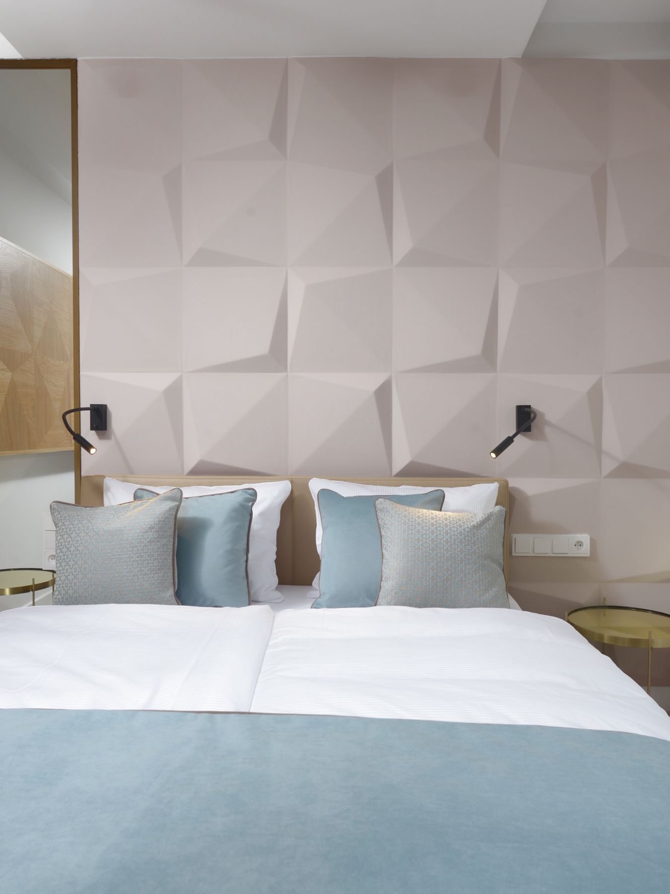 Een moderne hotelkamer met een wand met een geometrisch patroon, een groot bed met veel kussens en twee bedlampjes.