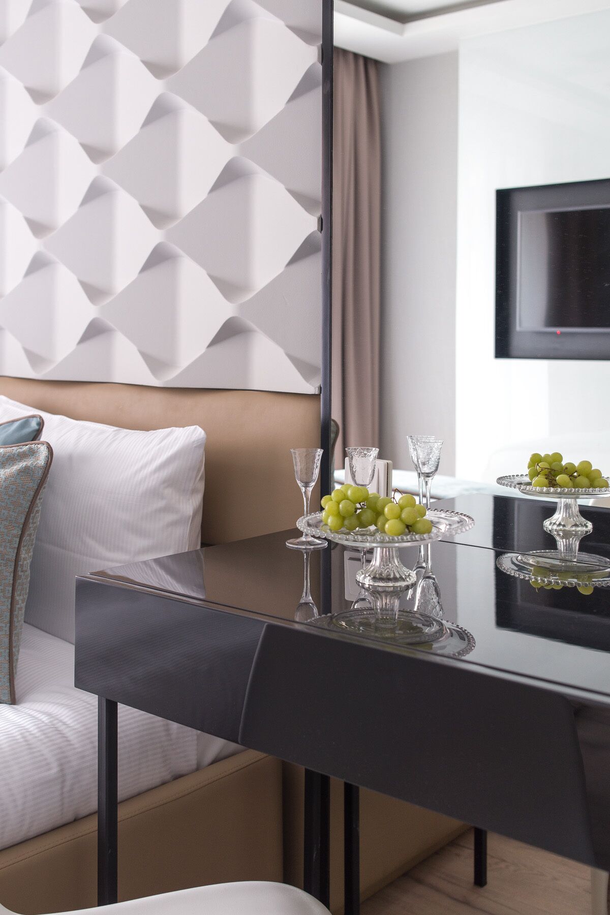 Habitación de hotel moderna con una mesa de comedor dispuesta para dos personas, con cubierta de vidrio y un centro de mesa decorativo de uvas verdes.