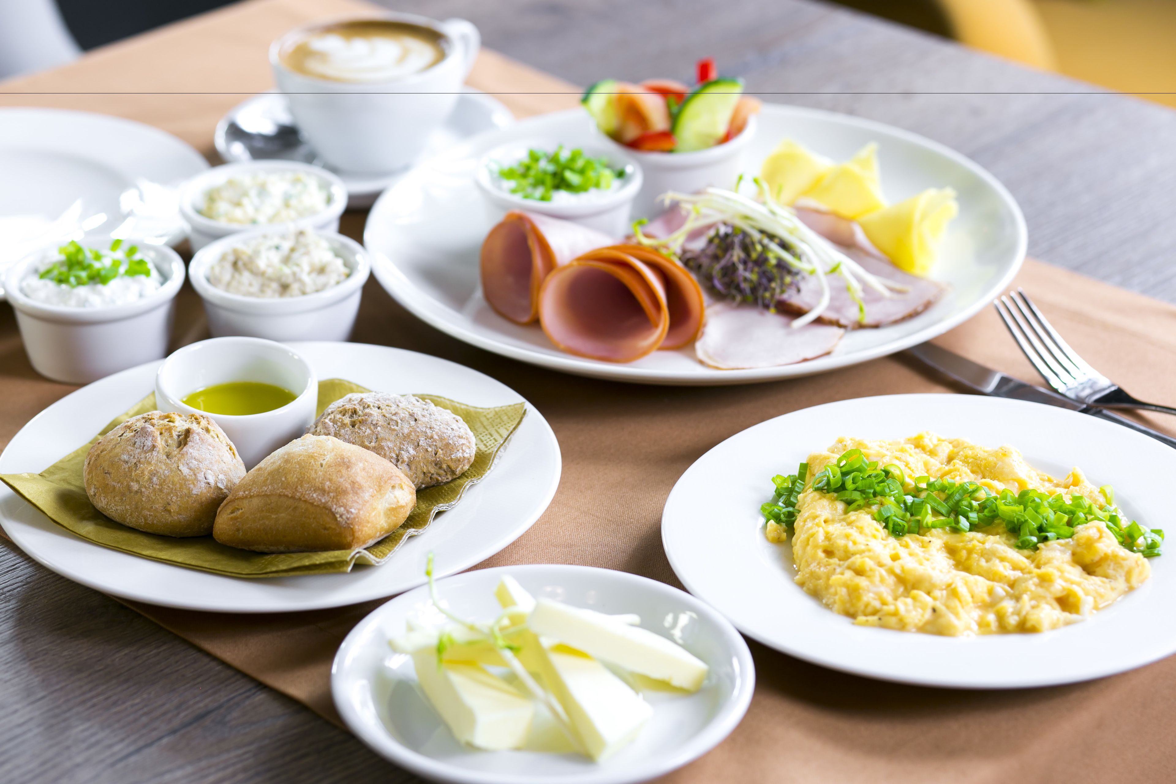 A table with various dishes including bread, cheese, and a plate of scrambled eggs.