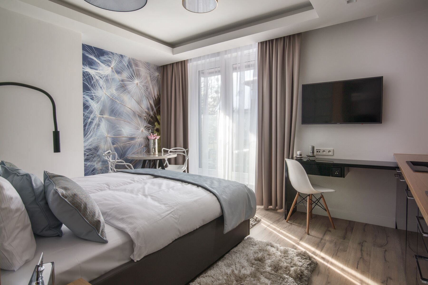 A modern bedroom with a bed, a desk, a chair, and a TV.