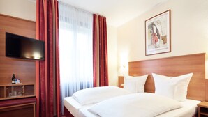 A hotel room with a bed, a TV mounted on the wall, a wooden headboard, and a poster on the wall. - Hotel Doria (Düsseldorf)