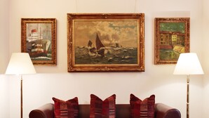 A living room with a red sofa, three framed paintings, and two floor lamps. - Hotel Doria (Düsseldorf)