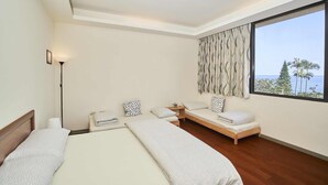 A modern hotel room with a large bed, a smaller sofa bed, a bedside table, and a view of the ocean. - Migratory Birds Hotel (Toucheng)