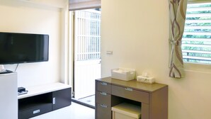 A hotel room with a flat-screen TV, a desk with drawers, a small table, and a window with blinds. - Migratory Birds Hotel (Toucheng)