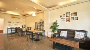 A modern living room with a sofa, coffee table, and dining area. There are framed pictures on the wall, a potted plant, and a small kitchen area in the background. - Migratory Birds Hotel (Toucheng)