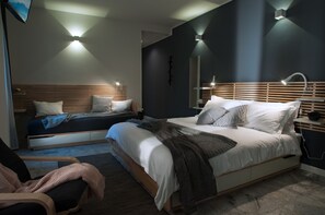Quarto moderno com cama grande, mesas de cabeceira, uma cadeira e televisão na parede.