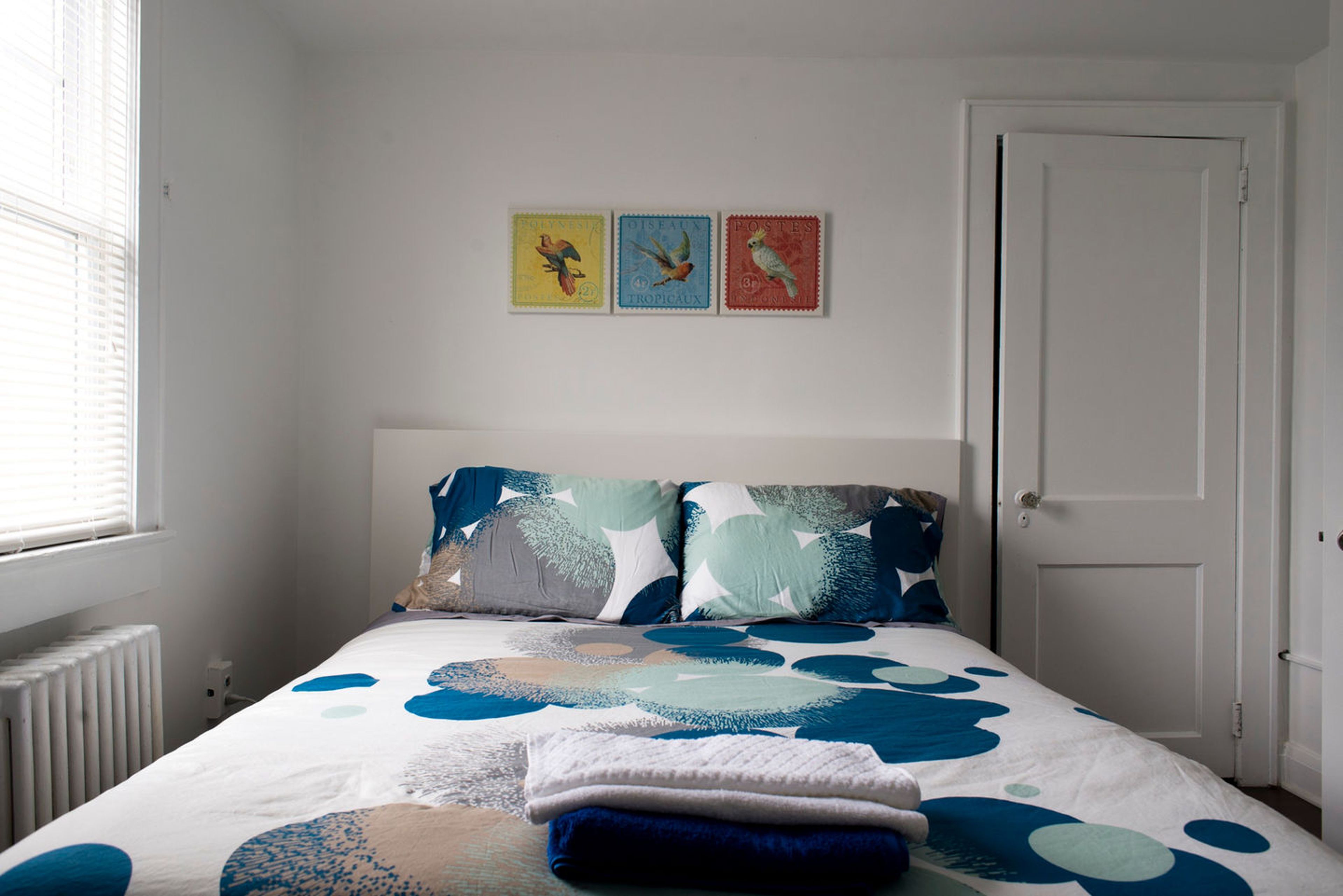 A bedroom with a bed, a radiator, a door, and three wall-mounted pictures.