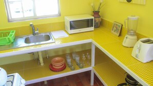 Una cocina con salpicadero de azulejos amarillos, un microondas blanco, un fregadero, un tostador y una licuadora.