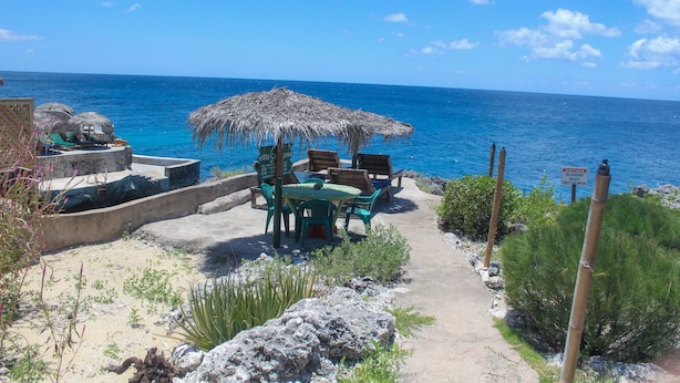 Un patio frente a la playa con sombrilla de paja, asientos al aire libre y vista al océano.