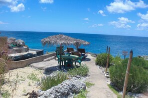 Eine Terrasse am Strand mit einem Reetdachschirm, Sitzgelegenheiten im Freien und Blick auf den Ozean.
