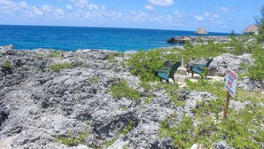 Una playa rocosa con un letrero que dice 'Propiedad Privada, Prohibido el Paso', una estructura de techo de paja y una silla.