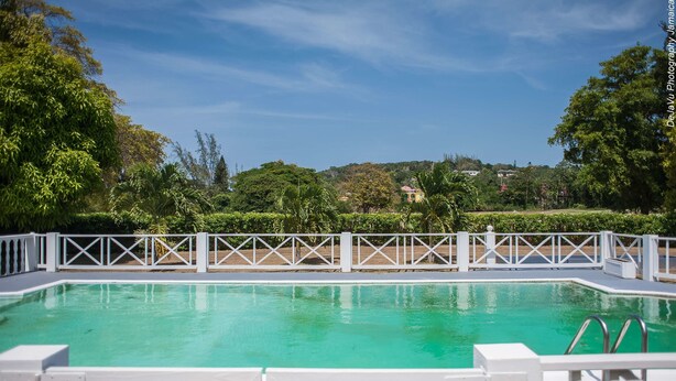 A rectangular swimming pool with a white deck and metal railings, surrounded by lush greenery and trees. - Breezy Shores at Cardiff Hall (Runaway Bay)
