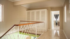 A staircase with a wooden handrail and white metal balusters, leading to a room with beige walls and a green carpet. - Breezy Shores at Cardiff Hall (Runaway Bay)