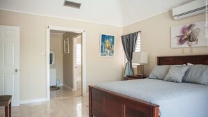 A bedroom with a large bed, a nightstand, a lamp, and a painting on the wall. - Breezy Shores at Cardiff Hall (Runaway Bay)