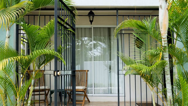 A balcony with a wooden chair, a metal gate, and lush green plants. - Wellington Cove (Kingston)
