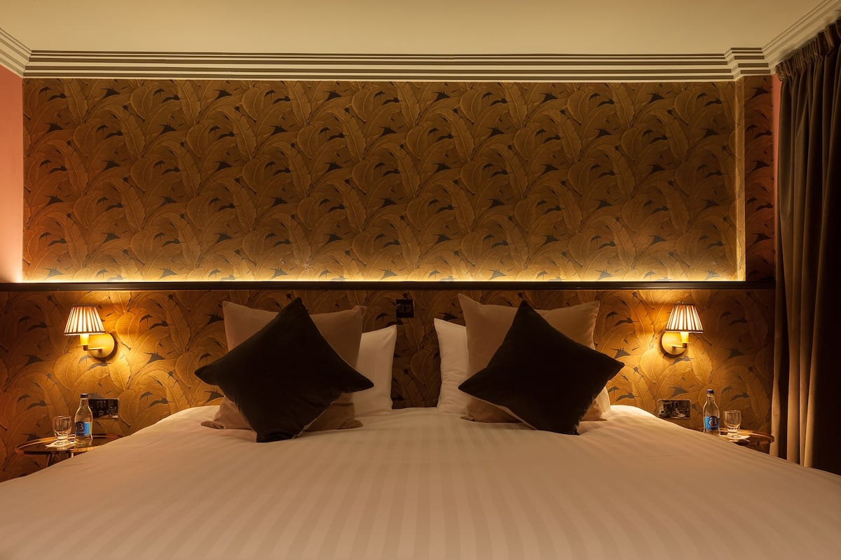 A hotel room with a large bed, two wall-mounted lamps, and a patterned wallpaper.
