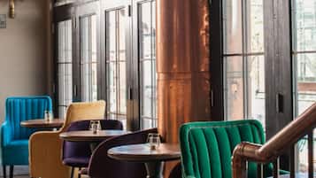 Interior de una cafetería con varias opciones de asientos, incluidas sillas y mesas, y ventanas amplias que dejan entrar luz natural.