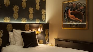 A hotel room with a bed, pillows, a nightstand, a framed painting, and pineapple-themed wall decor.