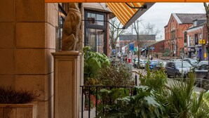 A stone building with a statue on the corner, a balcony with plants, and a street view with cars and buildings in the background. - House Hotel Belfast (Belfast)