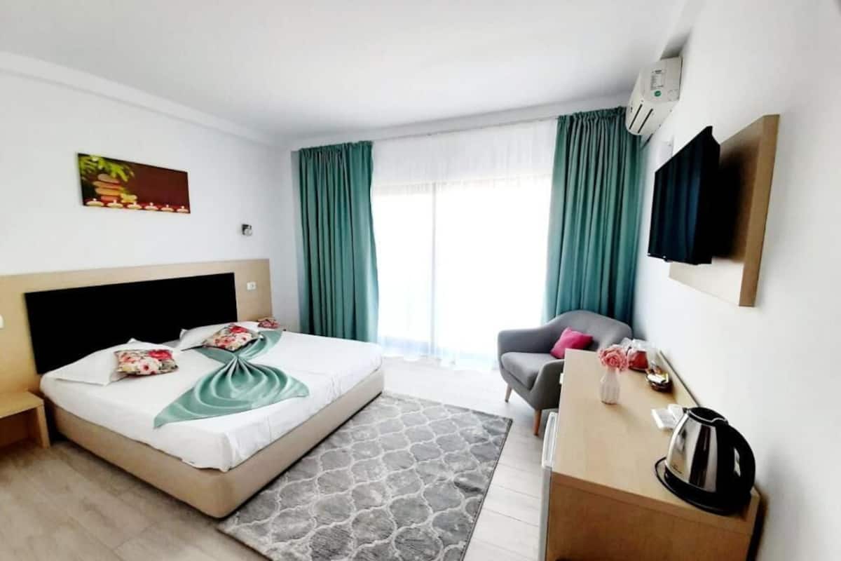 Ein Hotelzimmer mit zwei Betten, einem Schreibtisch, einem Stuhl, einem Fernseher und einem Fenster mit Vorhängen.