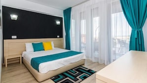 Une chambre d’hôtel avec un lit, une petite table de chevet, un bureau et une vue sur l’extérieur à travers des rideaux transparents.