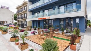Un hôtel doté d’une façade moderne, d’un espace extérieur aménagé avec des meubles en osier et des plantes en pot.