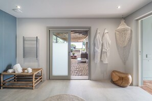 A modern bathroom with a wooden bench, a hanging light fixture, and a view of the outdoor patio. - Fazenda Nova - Country House (Tavira)