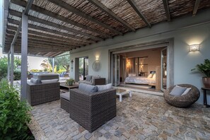 Un espace extérieur aménagé, abrité et doté de mobilier en osier, d’un sol en pierre et offrant une vue sur l’intérieur.