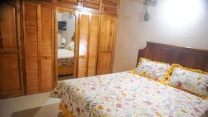 A bedroom with a floral bedspread, wooden wardrobe, and a mirror. - Eagles Nest (Montego Bay)