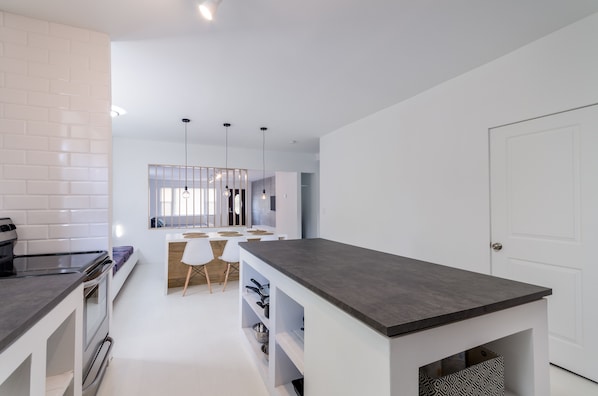 A modern kitchen with white cabinetry, a dark countertop, and a dining area with white chairs and a wooden table.