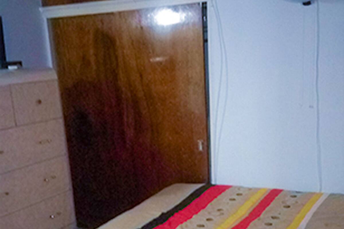 Une chambre avec deux lits, une armoire en bois et un ventilateur fixé au mur.