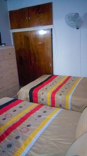 A bedroom with two beds, a wooden wardrobe, and a wall-mounted fan.