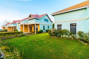 A row of pastel-colored houses with red roofs, a well-maintained lawn, and a clear sky.