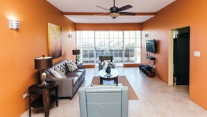 A living room with a sofa, armchairs, a coffee table, a TV, and a ceiling fan. - Paradise  Beach Front Apartment (Discovery Bay)