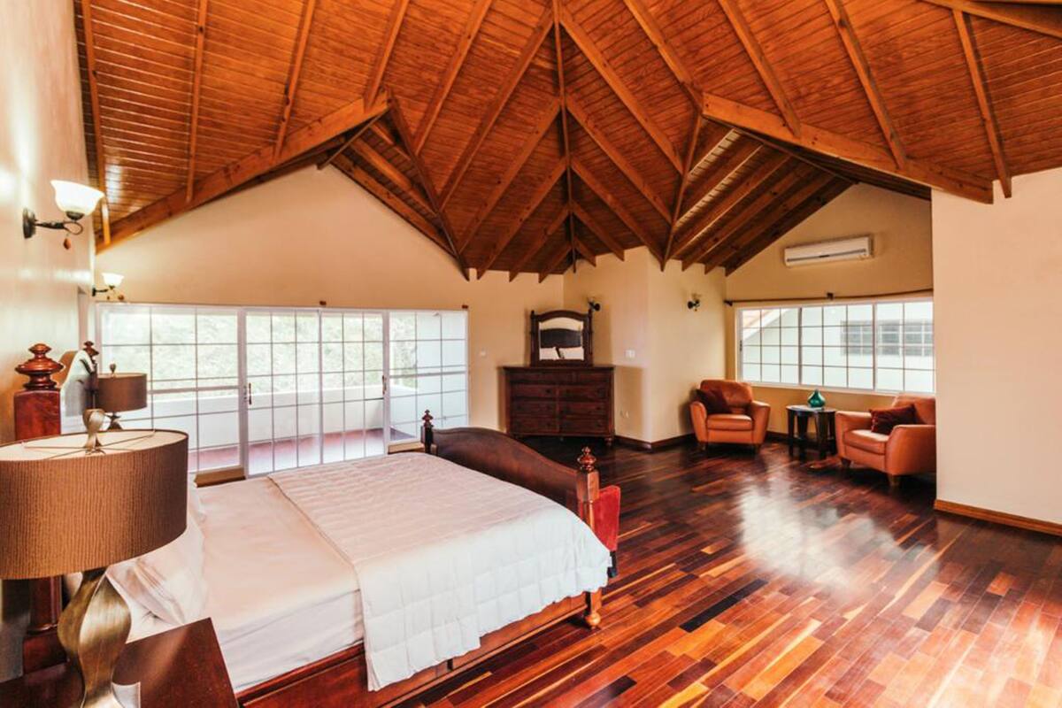 Ein geräumiges Schlafzimmer mit einem großen Bett, Holzböden, einer schrägen Decke und großen Fenstern.