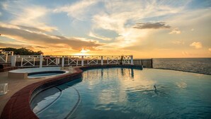 A swimming pool with a view of the sunset over the ocean, a wooden deck, and a fence. - Paradise  Beach Front Apartment (Discovery Bay)